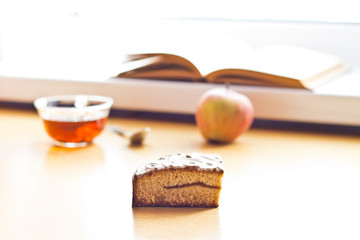 Still life composition: book tea apple cake. With selective focus and blurred background. Sunlight from window