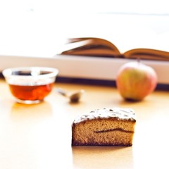 Still life composition: book tea apple cake. With selective focus and blurred background. Sunlight from window