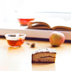 Still life composition: book tea apple cake. With selective focus and blurred background. Sunlight from window