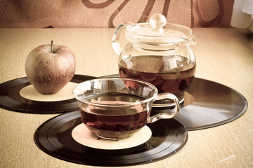 Morning musical tea in glass cup and teapot with ripe apple on vinyl records. Blurred background. Image with vintage filter and vignette