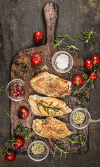 Roasted chicken breast with fried herbs and tomatoes on rustic cutting board, top view