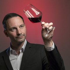 man tasting red wine in jacket in front of red background