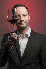 man tasting red wine in jacket in front of red background