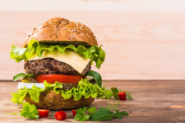 Big hamburger with beef cutlet and vegetables on wood plate