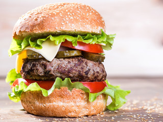 Big hamburger with beef cutlet and vegetables on wood plate