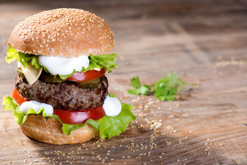 Big hamburger with beef cutlet and vegetables on wood plate
