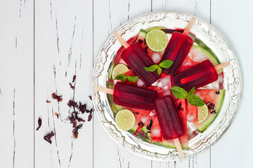 Refreshing mexican style popsicles with watermelon, hibiscus, lime on vintage silver tray with watermelon slices, lime and mint leaves. Cinco de Mayo agua fresca recipe