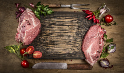 Raw pork meat chops with kitchen tools, fresh seasoning and ingredients for cooking on rustic wooden background, top view, frame. Place for text.
