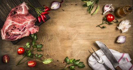 Pork kotelett with fresh ingredients for cooking - herbs,spices and tomatoes. Vintage kitchen tools - fork and meat knife. Rustic wooden backgound, top view, frame