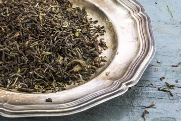 loose black Darjeeling Tea on a silver plate on rustic blue pain