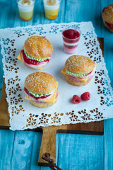 Sweet cake in the form of a burger, strawberry mousse with white chocolate and roll with sesame seeds, cooking background