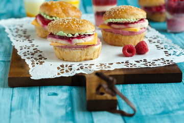 Sweet cake in the form of a burger, strawberry mousse with white chocolate and roll with sesame seeds, cooking background