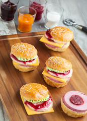 Sweet cake in the form of a burger, strawberry mousse with white chocolate and roll with sesame seeds, cooking background