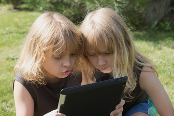 Two blond boys are playing with the tablet outdoors