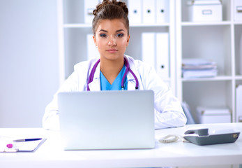 Female doctor sitting on the desk and working a laptop in