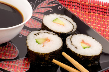 Sushi on a black plate on a red mat with chopsticks