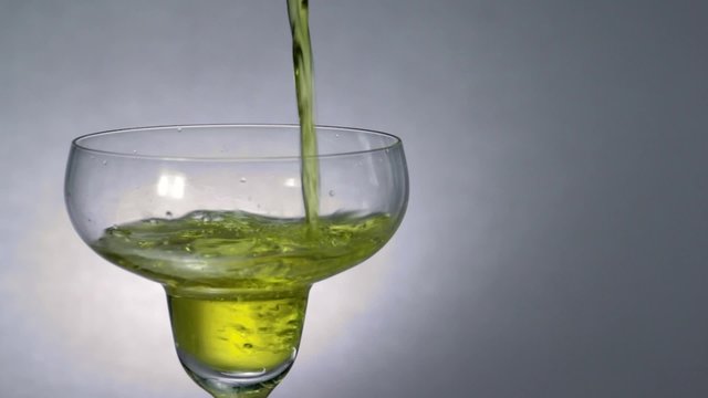 Yellow drink is poured into cocktail glass