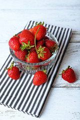 Ripe strawberries in glass saucer on napkin on wooden table, closeup