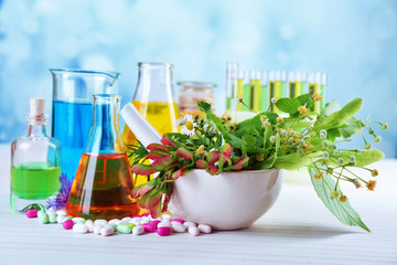 Herbs in mortar, test tubes and pills,  on table, on light background