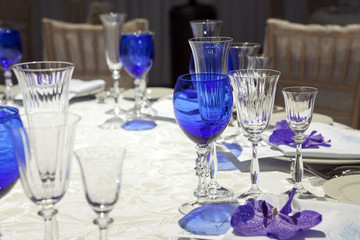 serviette on a plate served on the festive table. Blue goblet and violet orchid