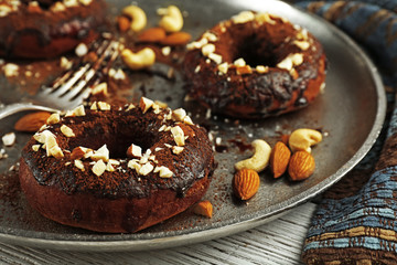 Delicious doughnuts with chocolate icing and nuts on table close up