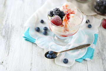 Delicious ice cream with fresh frozen berries and sauce, on color wooden background