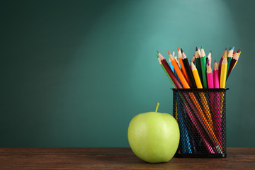 metal holder with crayons and green apple on desk on green chalkboard background - Powered by Adobe