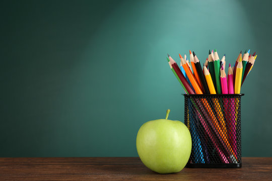metal holder with crayons and green apple on desk on green chalkboard background