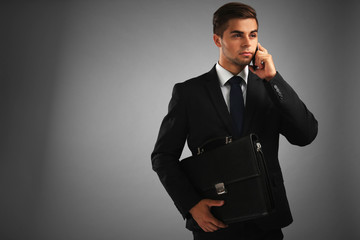 Elegant man in suit with briefcase on gray background