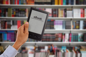 Male’s Hand holding empty e-book with library shelfs in backgr