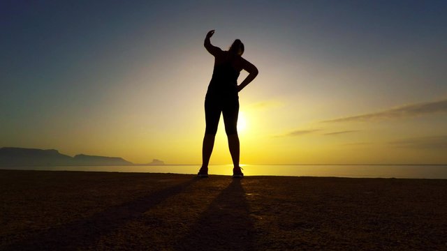 Young woman doing yoga on the beach at sunrise in Spain. Silhouette against rising sun.