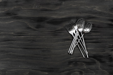 Some spoons and forks on a black wooden surface