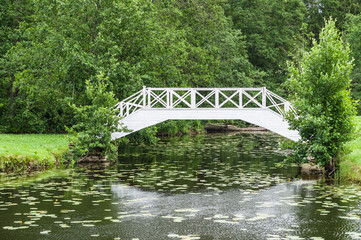 Decorative white wooden bridge over small pond in park