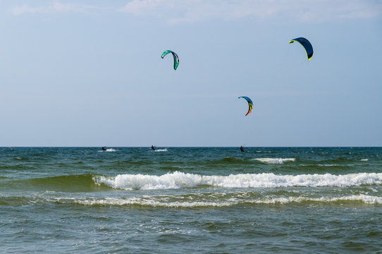 Silhouettes of three kiters ride on the waves of sea