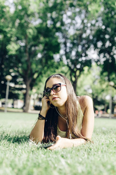 Beautiful young woman lying on the grass in a park with a smart