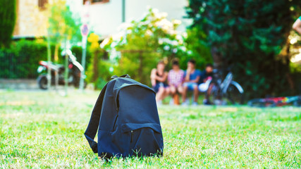 Blue school backpack standing on green grass with students in ba