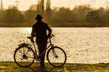 Fototapeta na wymiar Mann mit Hut und Fahrrad blickt über See in die Ferne