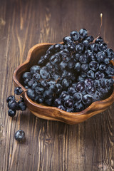 Black grapes in a wooden bowl on brown rustic table. Selective focus. Vintage style