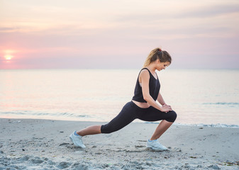 Fototapeta na wymiar Fitness sport model smiling happy doing exercises during outdoor work out on sunrise. Beautiful caucasian female training outside on seaside in the morning