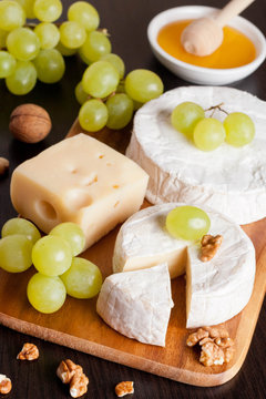 cheeses, honey, grapes and walnuts on a wooden background