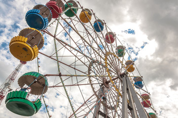 Ferris wheel. Attractions in amusement park. Clouds in sky and colorful cabins.