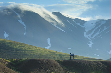 Two hikers on the Laugavegur during a tranquil and cloudy summer sunrise on Iceland.