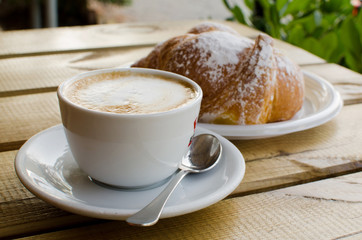 The cup of cappuccino with croissant in the background - tipical