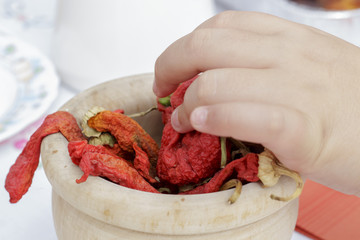 The hand of a boy taking a dry spicy pepper from a wooden bowl