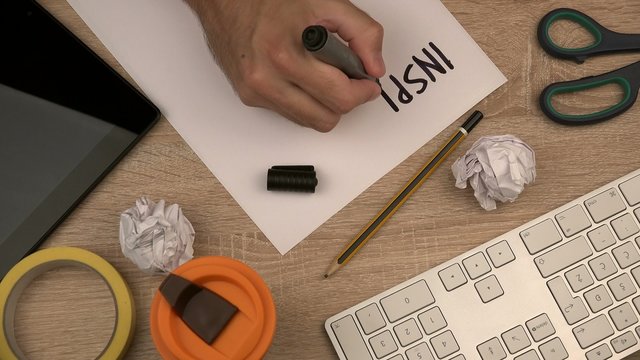 Businessman writing word Inspiration on piece of paper at workplace, office desktop top view, tabletop in design studio, 4k uhd footage 2160p.