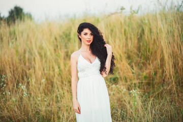 Fototapeta na wymiar beautiful young girl in a field in white dress has beautiful lon