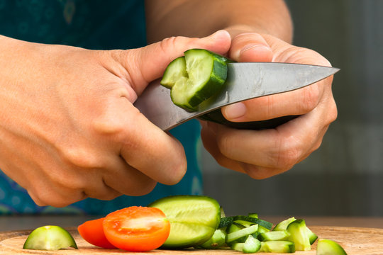 hands chopping cucumber for salad, closeup