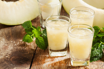 Melon juice in a glass, mint  and slices of melon on a wooden ba