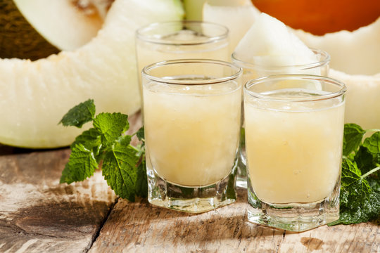 Melon juice in a glass, mint  and slices of melon on a wooden ba