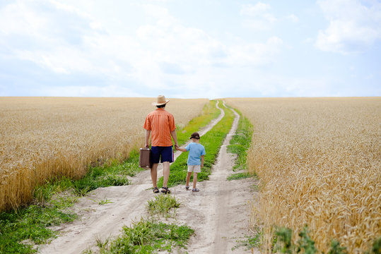 Man With Suitcase And Boy Walking Away In Wheat Field